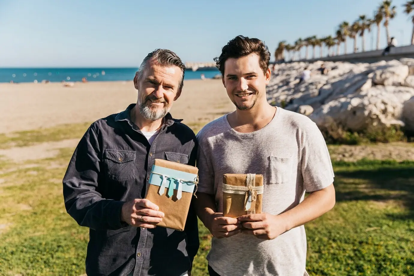 A father and son pose at the beach with a gift.